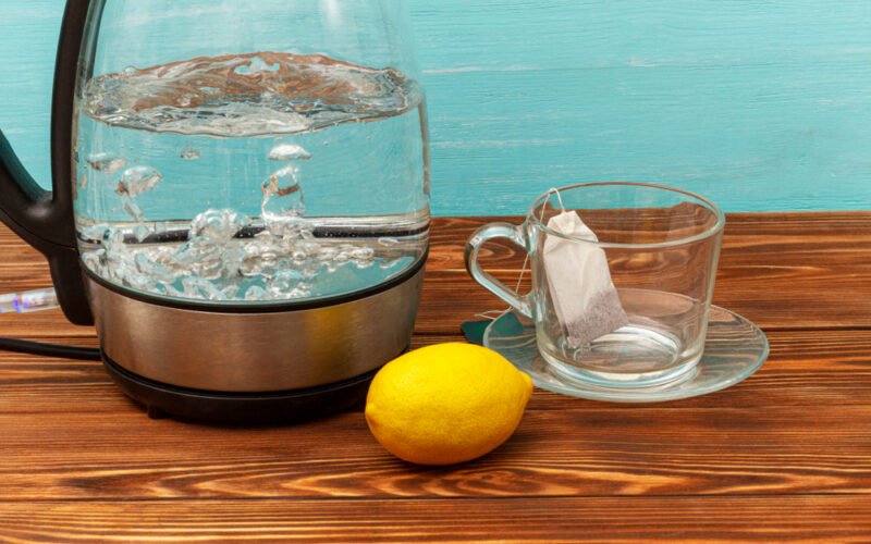 Vriaca sklenená kanvica, vedľa citrón a šálka s čajovým sáčkom