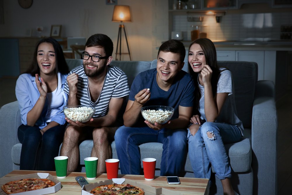 4 mladí ľudia s pukancami pred televízorom