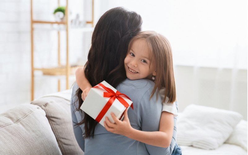 Dievčatko s darčekom v ruke objíma svoju mamu