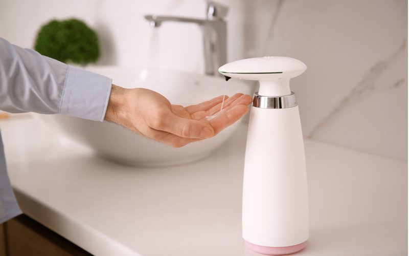 Muž si dávkuje mydlo pomocou bieleho bezdotykového dávkovača