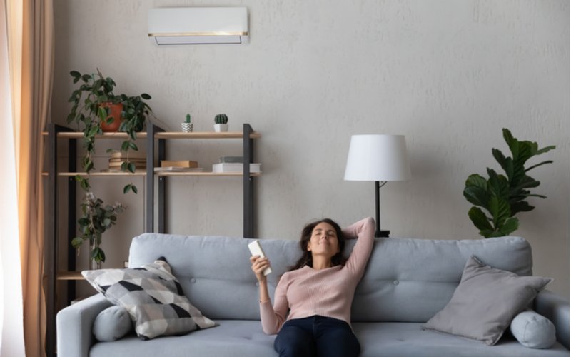 Kúrenie klimatizáciou - žena na gauči zapína klimatizáciu