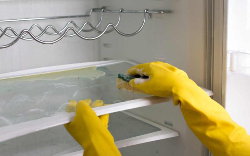 Ruky v rukaviciach čistia vnútro chladničky