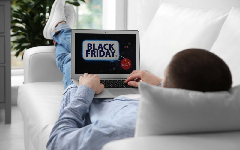 Black Friday 2023 - muž nakupuje z pohodlia gauča online pomocou notebooku, detail